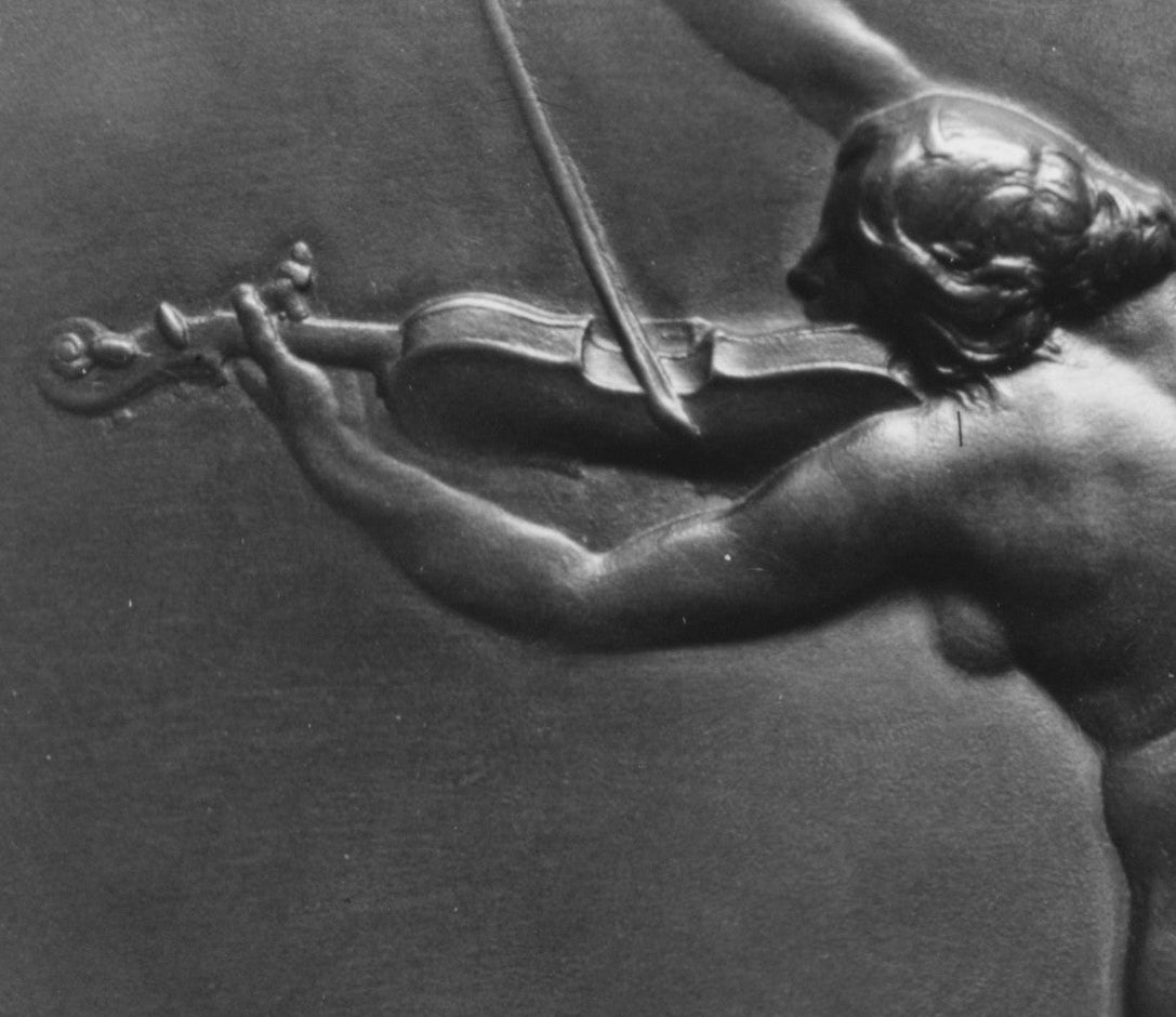 Relief sculpture of a nude figure playing a violin on a dark background