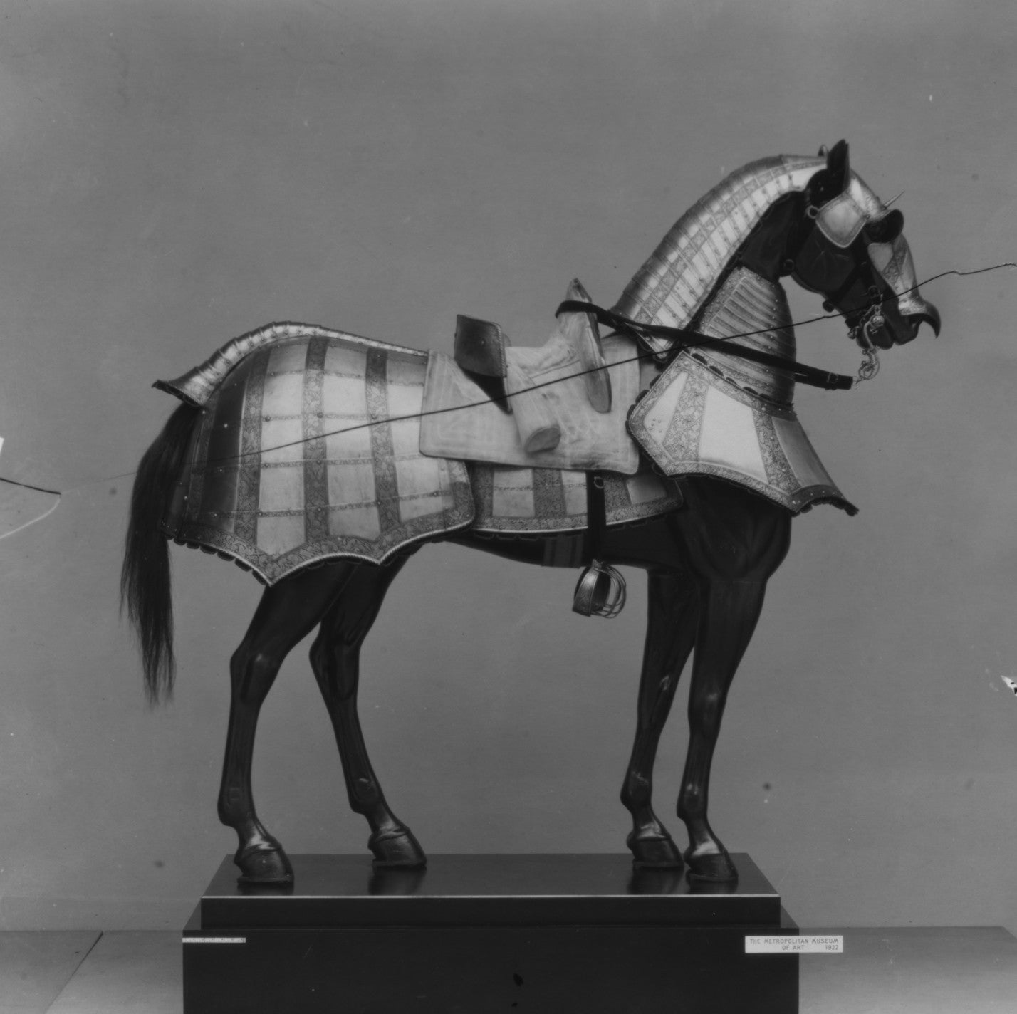 Black and white model of a horse with a plaid saddle blanket on a gray background