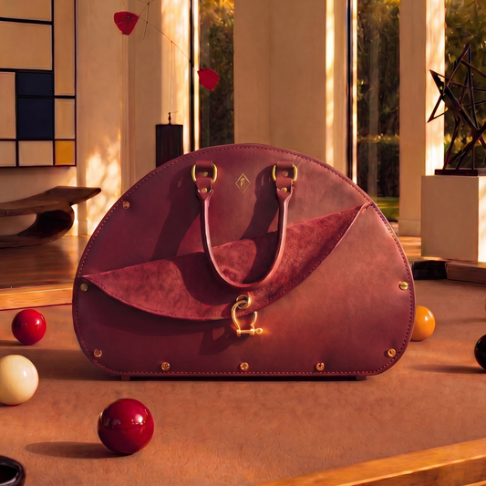 Oxblood handbag on a pool table with pool balls and fine art around